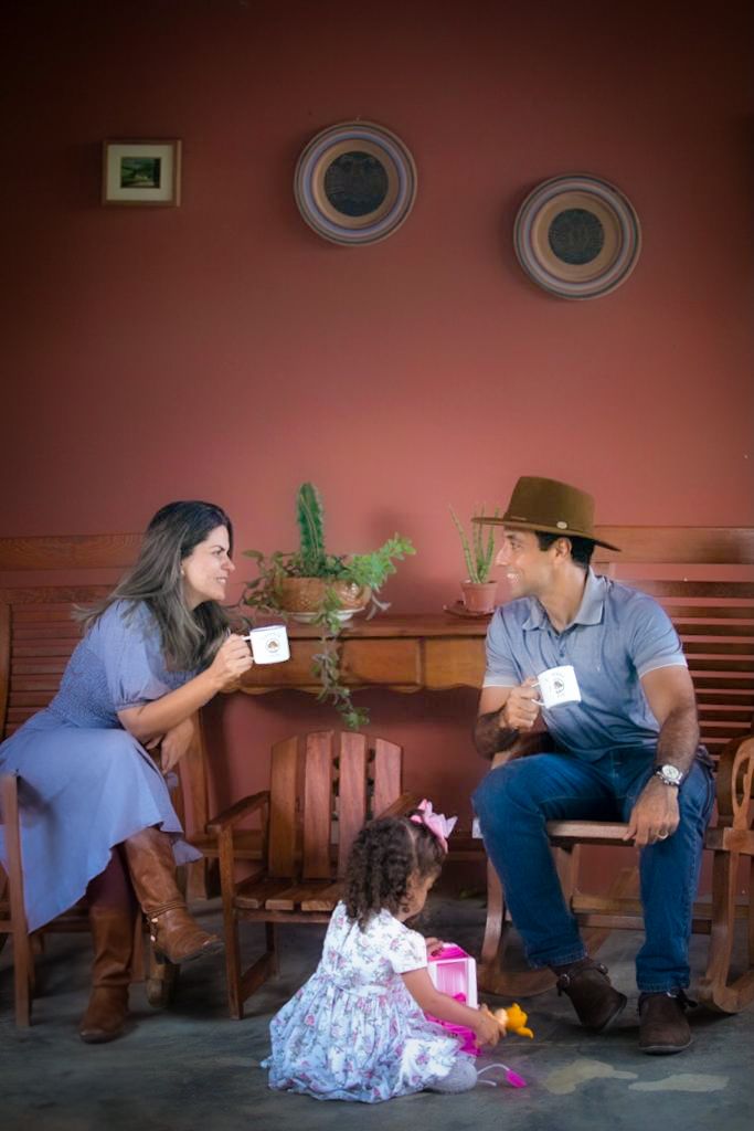 Casal tomando café na varanda enquanto a filha brinca